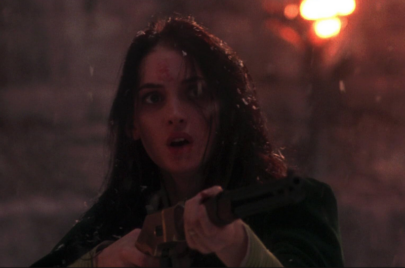 Winona Ryder as Mina, in snow and dusk, holds a gun pointed slightly to the right of the camera, fearfully but determinedly, eyes wide, lips parted, red burn clearly visible on her forehead. Detail of still from Bram Stoker's Dracula (1992).